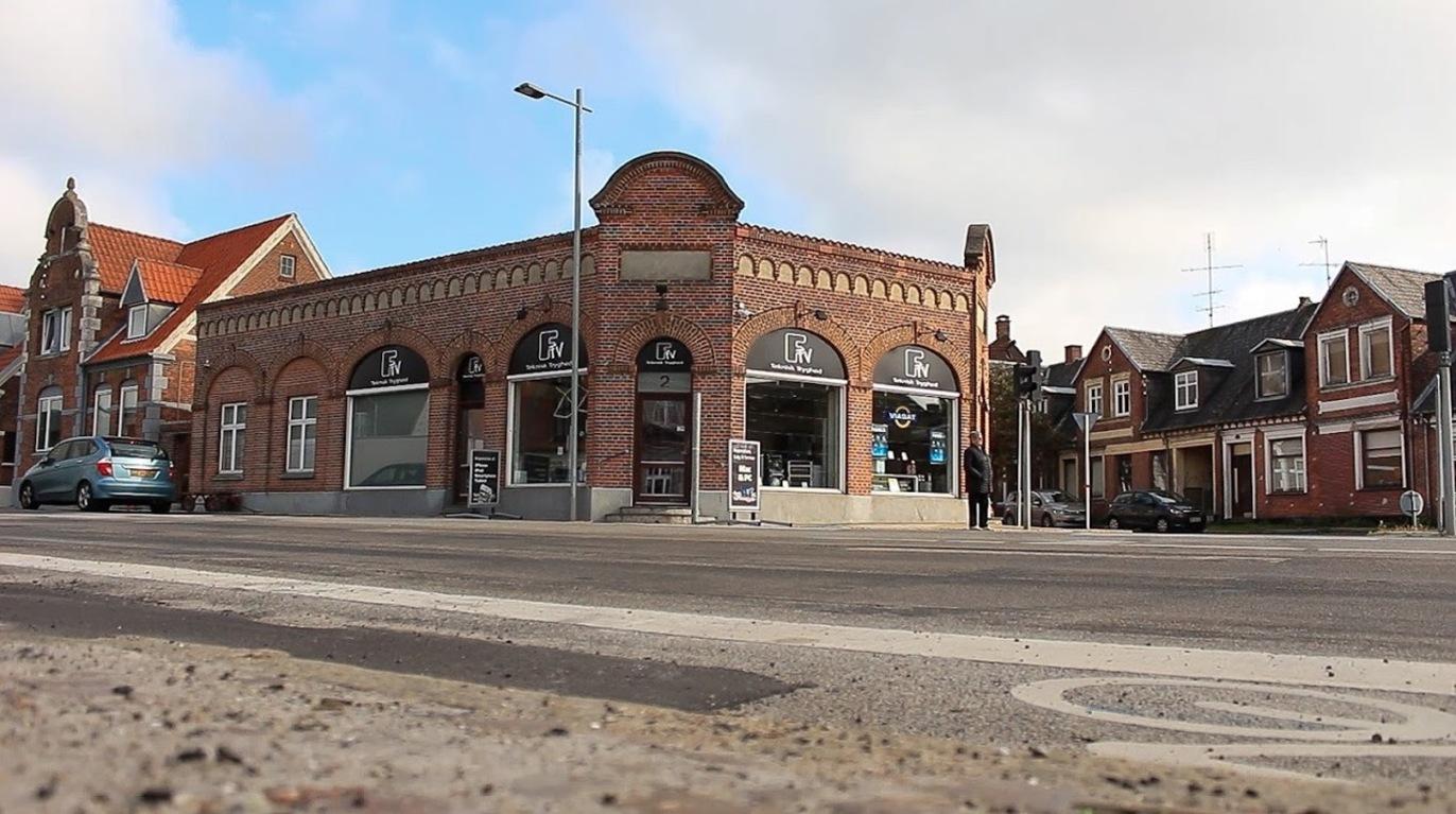 En murstensbygning med store vinduer og en buet facade, beliggende på et gadehjørne i en by.
