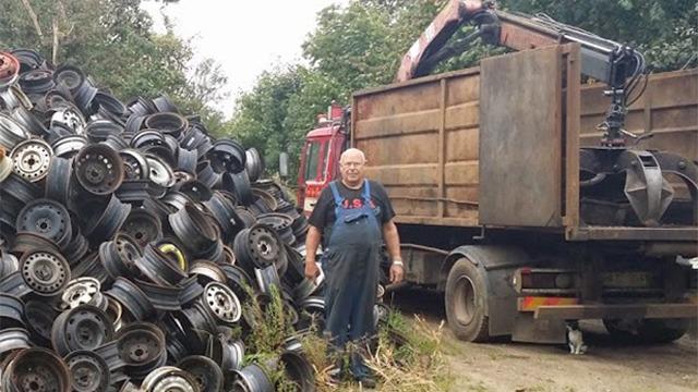 En mand står ved en bunke af gamle dæk ved en lastbil i en skrotplads.