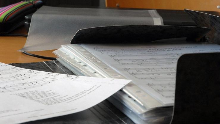 Et nærbillede af et musikmappe med noder og papirer på et skrivebord.