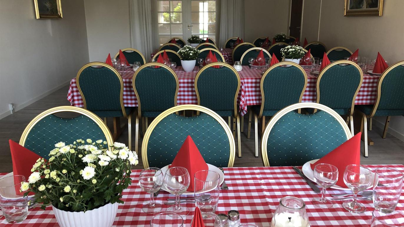 Dækning af et festlokale med ternet dug, grønne stole, røde servietter og blomster i potter.