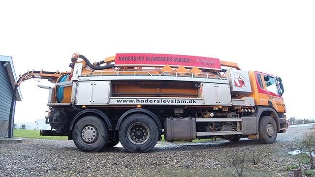 En stor lastbil med en rød og orange kran, der står på en grusvej ved en bygning.