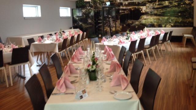 Elegant festlokale med dækkede borde, lyserøde servietter og blomsterdekorationer til en festlig begivenhed.