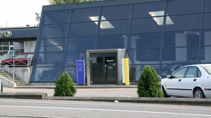 Moderne bygning med glasfacade, indgang og parkerede biler foran.