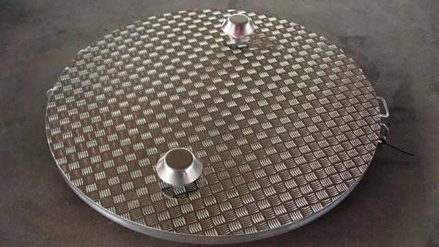 Et rundt metalmanhole dække med en diamantmønster overflade og to håndtag på toppen.
