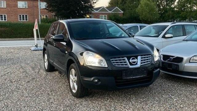 En sort Nissan SUV parkeret på en grusplads med andre biler i baggrunden.