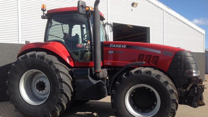 Rød traktor fra Case IH med store dæk, parkeret foran en lagerbygning.