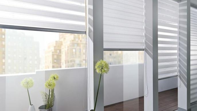Moderne persienner i et lyst rum med planter og udsigt til byen.