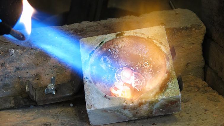 Flamme fra en gasbrænder smelter metal i en form lavet af sten.