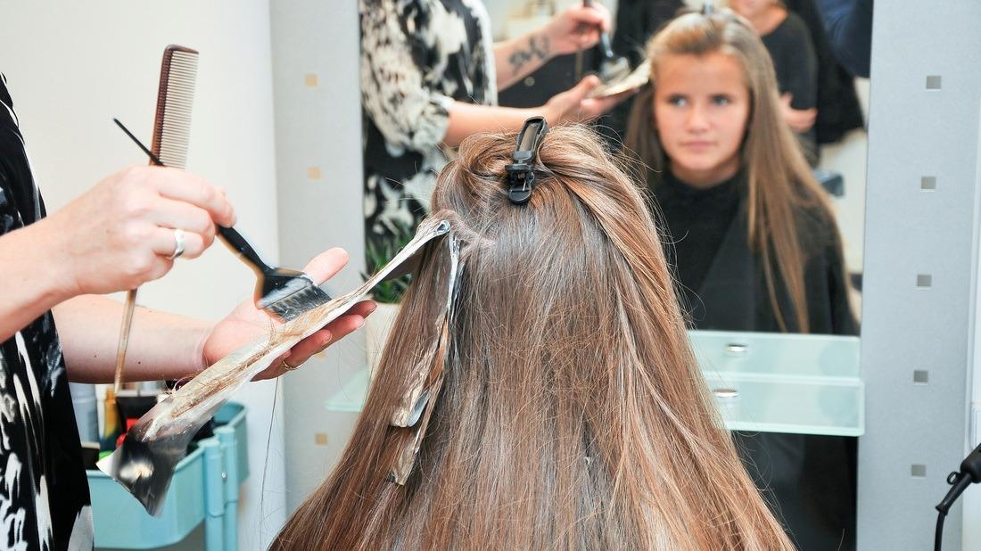 En frisør farver hår på en kunde i en salon, mens kunden ser sig selv i spejlet.