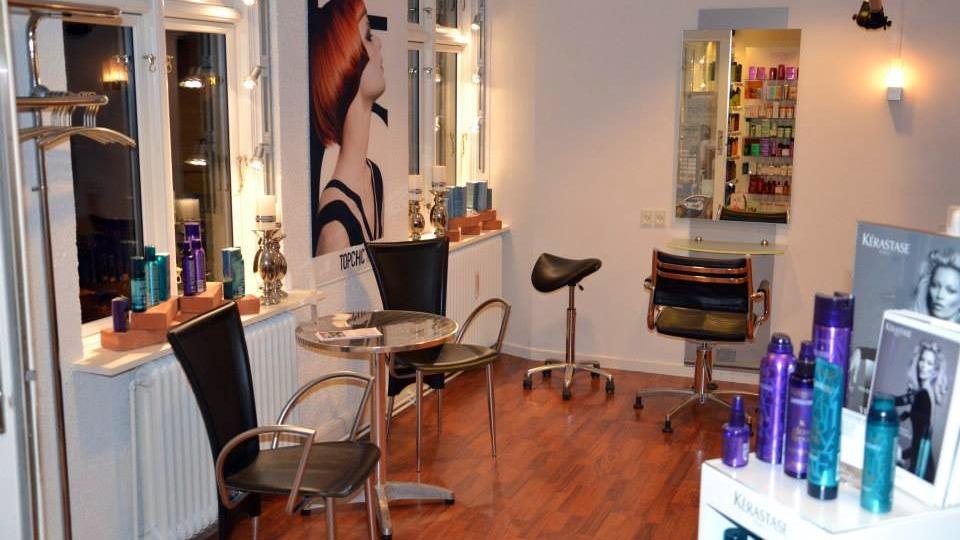 En moderne frisørsalon med stole, spejl og hårprodukter på hylderne.