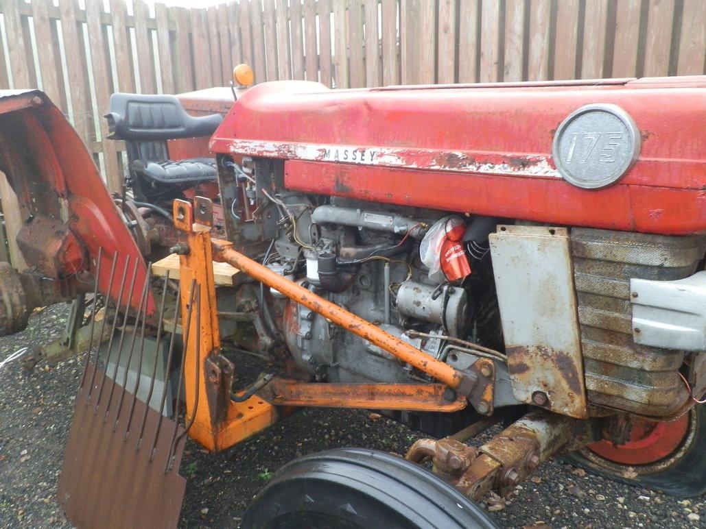 Rød traktor med slidt karrosseri og orange frontlæsser, parkeret ved et hegn.