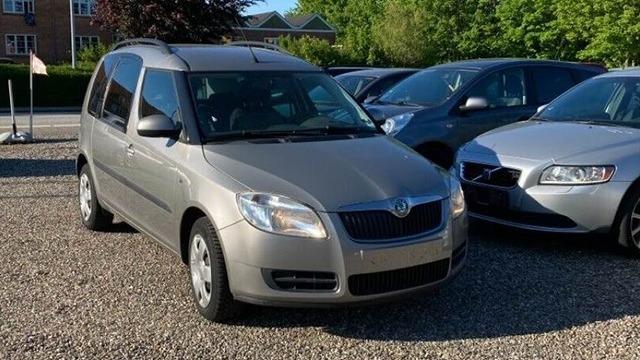 En sølvgrå bil parkeret blandt andre biler på en grusplads. Bilen har en rummelig krop og moderne design.