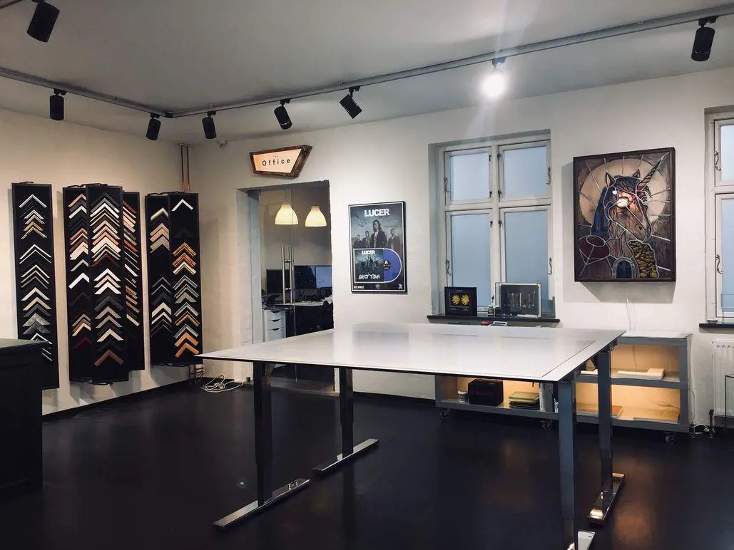 Moderne indretning af et kunstnerisk rum med rammer, malerier og et stort bord i midten.