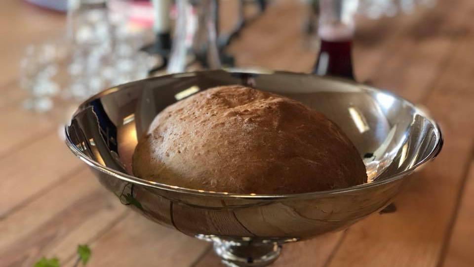 En nybagt brød i en skål af rustfrit stål på et træbord, omgivet af dekorative elementer.