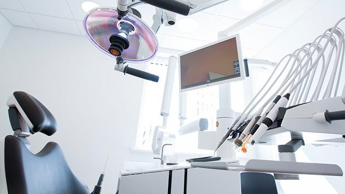 Moderne tandlægeklinik med tandlægestol, lys og udstyr til behandling.