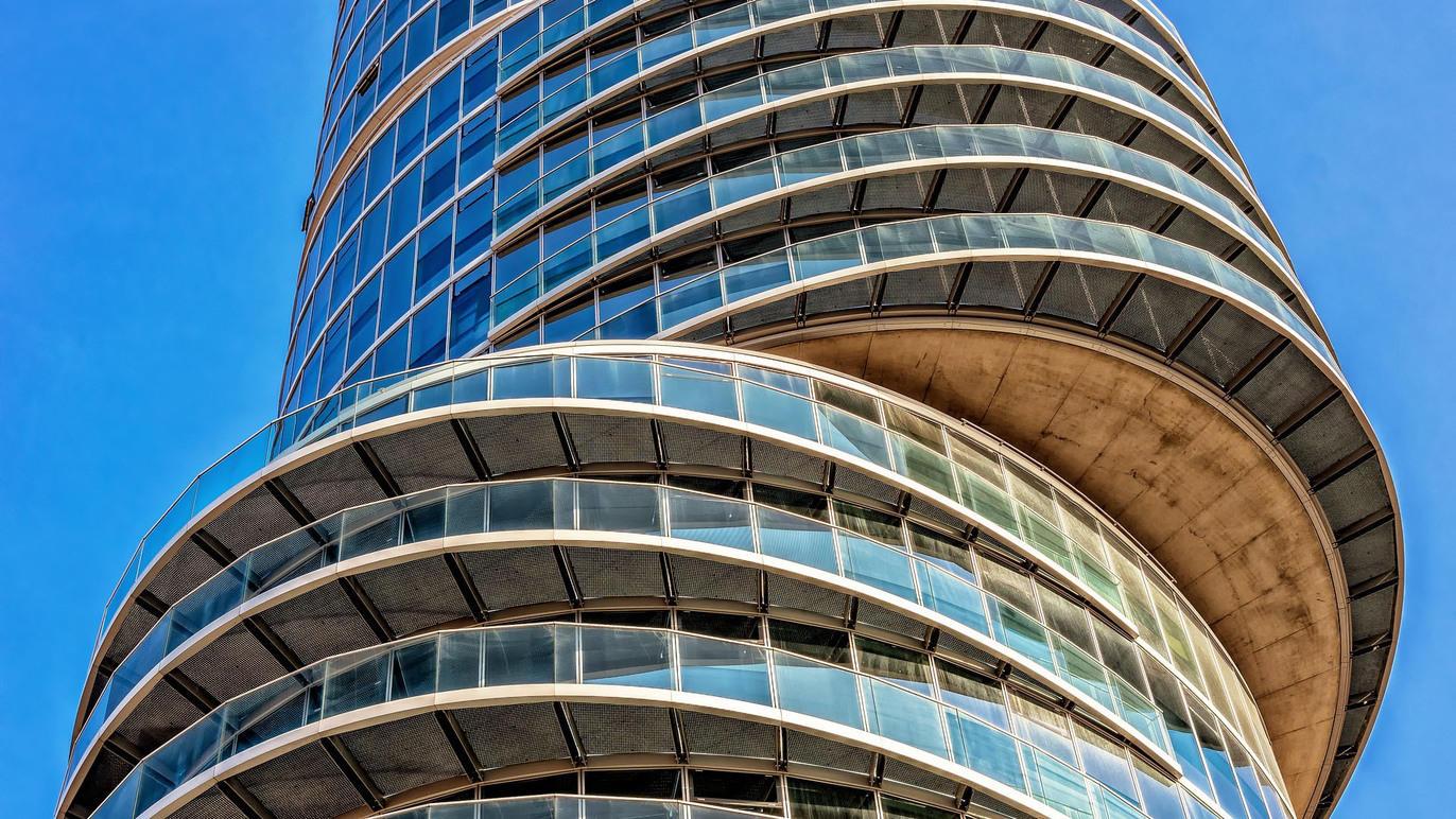 Moderne bygning med spiralformet design og store glasvinduer under en klar blå himmel.