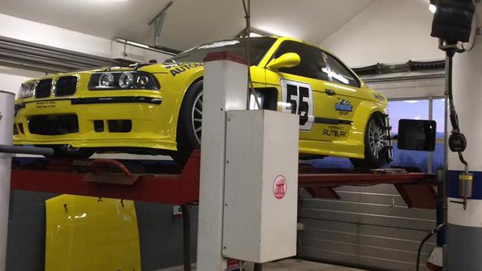 En gul racerbils BMW på en løftebænk i et garageværksted. Bilen har nummer 55 og racingdekor.