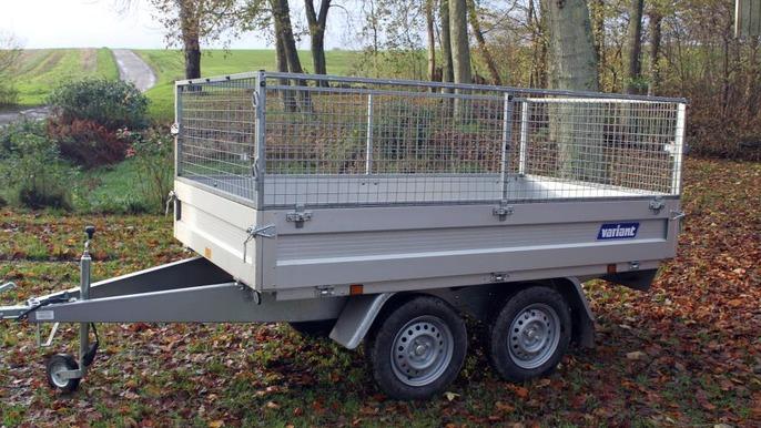 En trailer med gitterhegn, parkeret på en græsplæne omgivet af træer og efterårsblade.