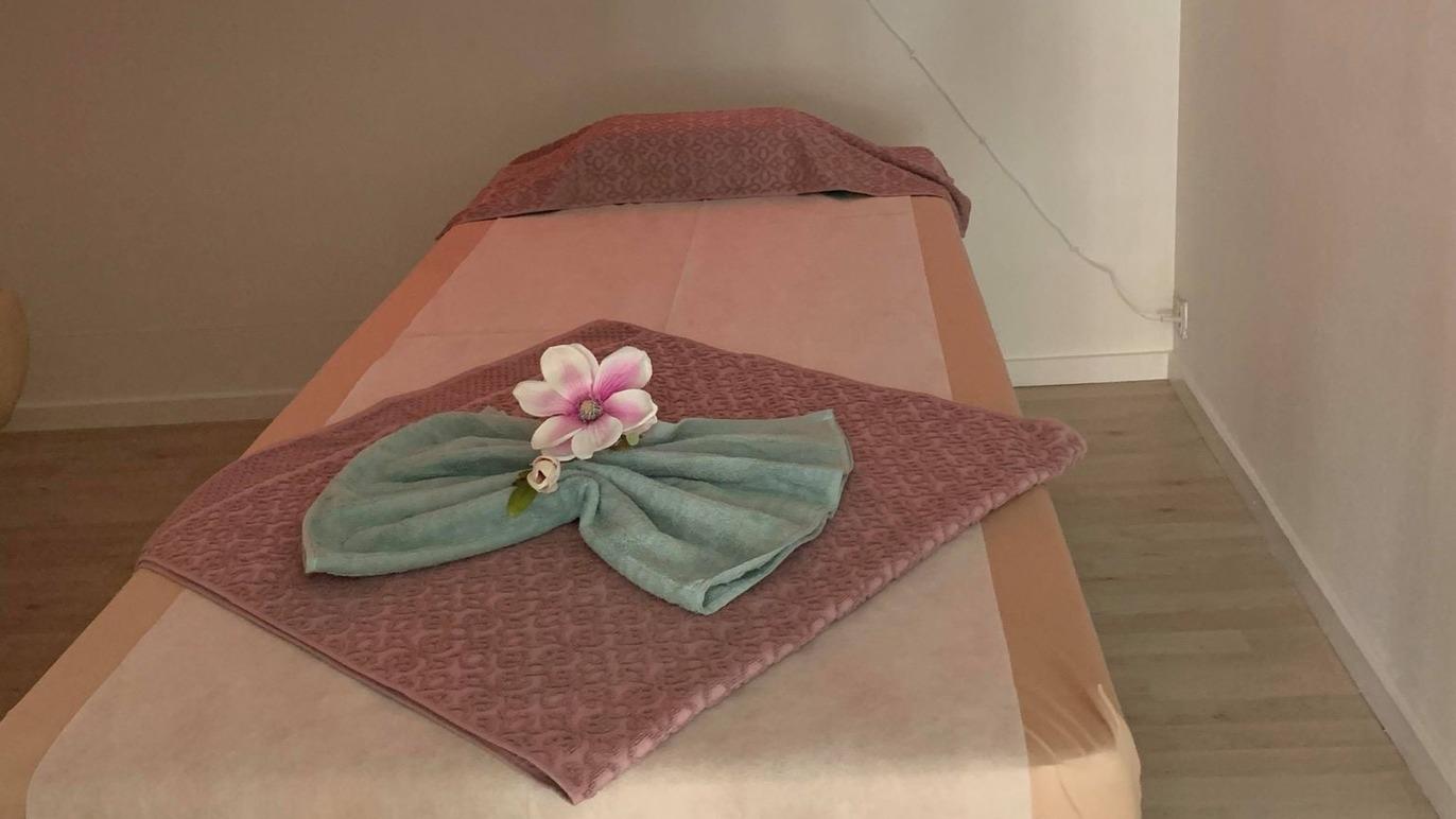 En massagebriks med en lyserød blomst og foldede håndklæder i en afslappende atmosfære.