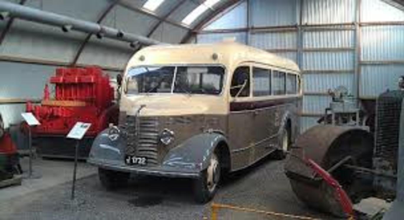 En gammel bus i et museum, omgivet af historiske maskiner og udstyr.