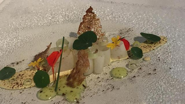 En elegant tallerken med gourmetmad, bestående af grøntsager, urter og blomsterdekorationer.