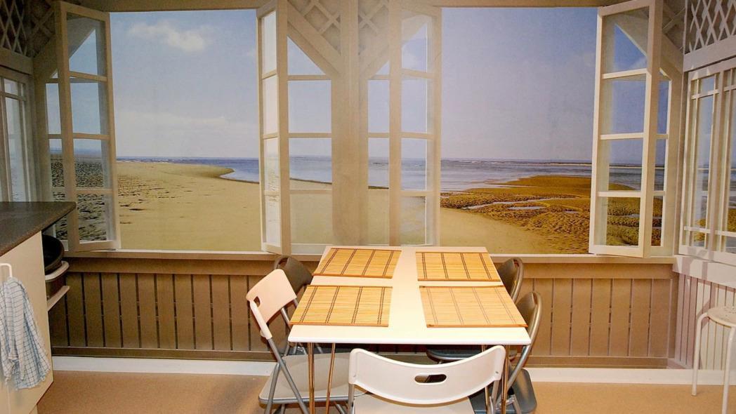 Lys og indbydende køkken med udsigt til strand og hav, bord med træplader og åbne vinduer.