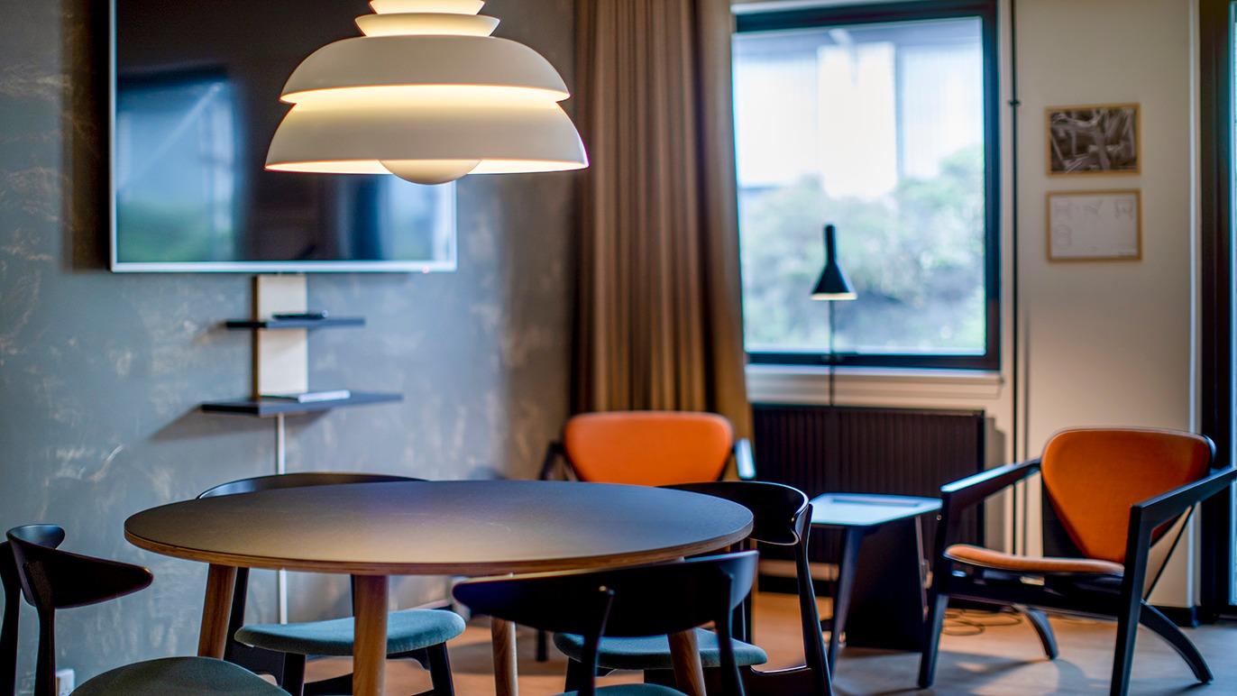 Moderne stue med et rundt bord, stilfulde stole og en stor lampe, der hænger over bordet.