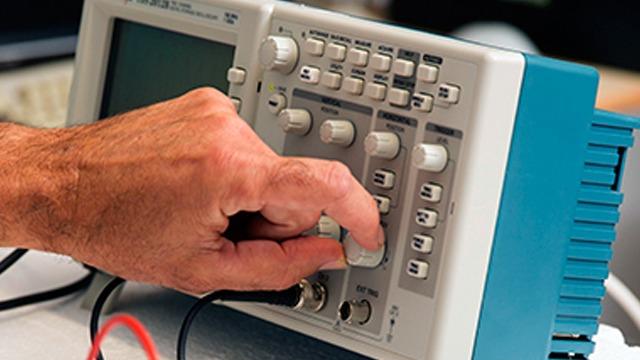 En hånd justerer indstillingerne på et elektronisk måleinstrument med knapper og skærm.