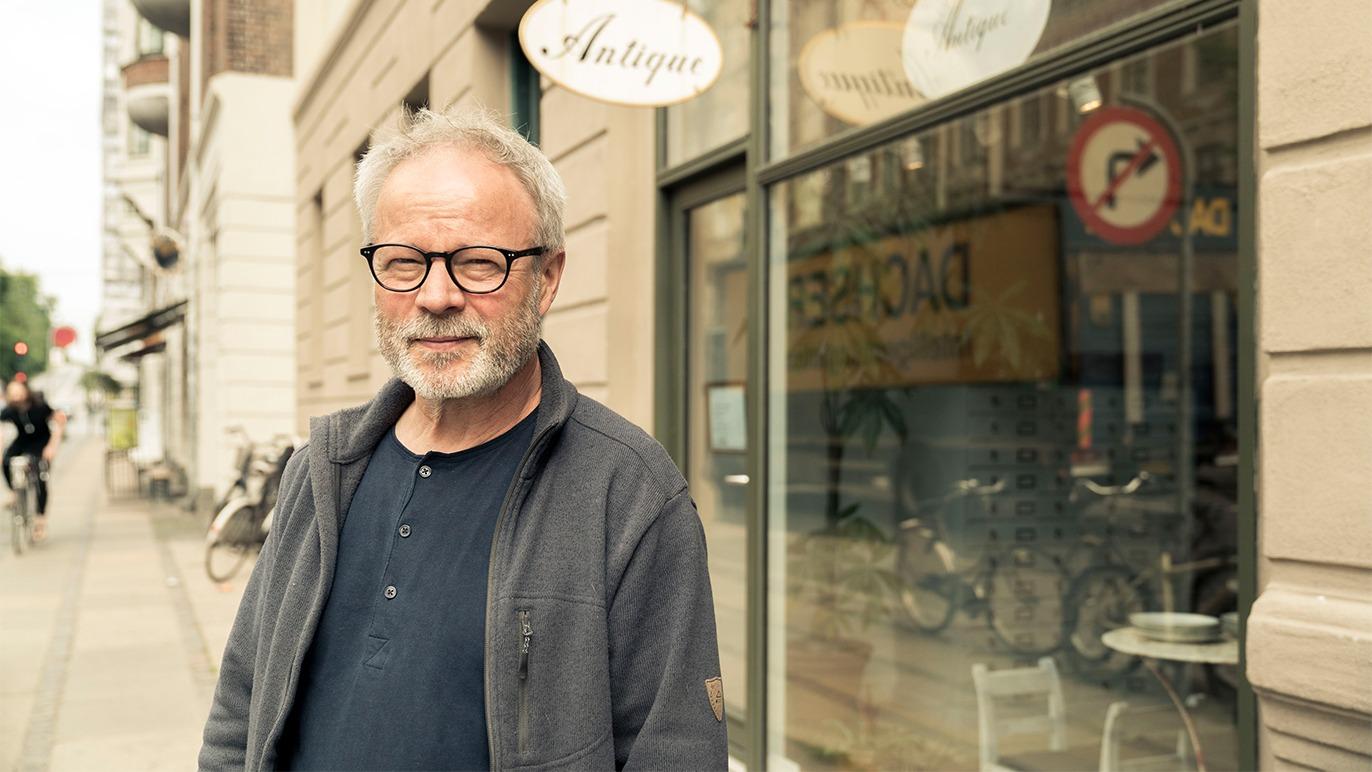 Mand med briller står foran en antikvitetsbutik på en gade i byen.