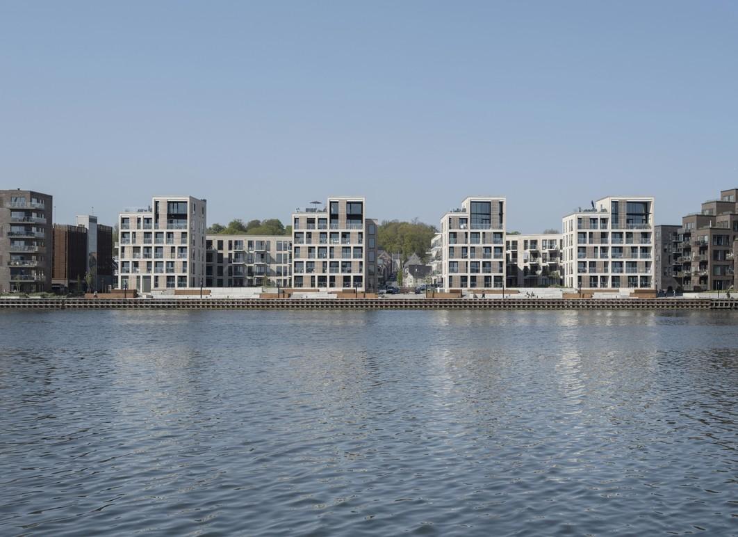 Moderne lejlighedsbygninger ved vandet med spejlbillede i roligt vand.