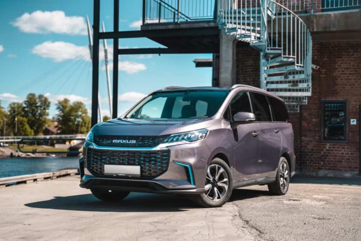 En moderne MPV parkeret ved en vandkant med en spiraltrappe i baggrunden. Bilen har en grå farve og et stilrent design.