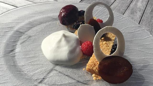 En elegant desserttallerken med skiver af frugt, flødeskum og små kager dekoreret med chokolade.