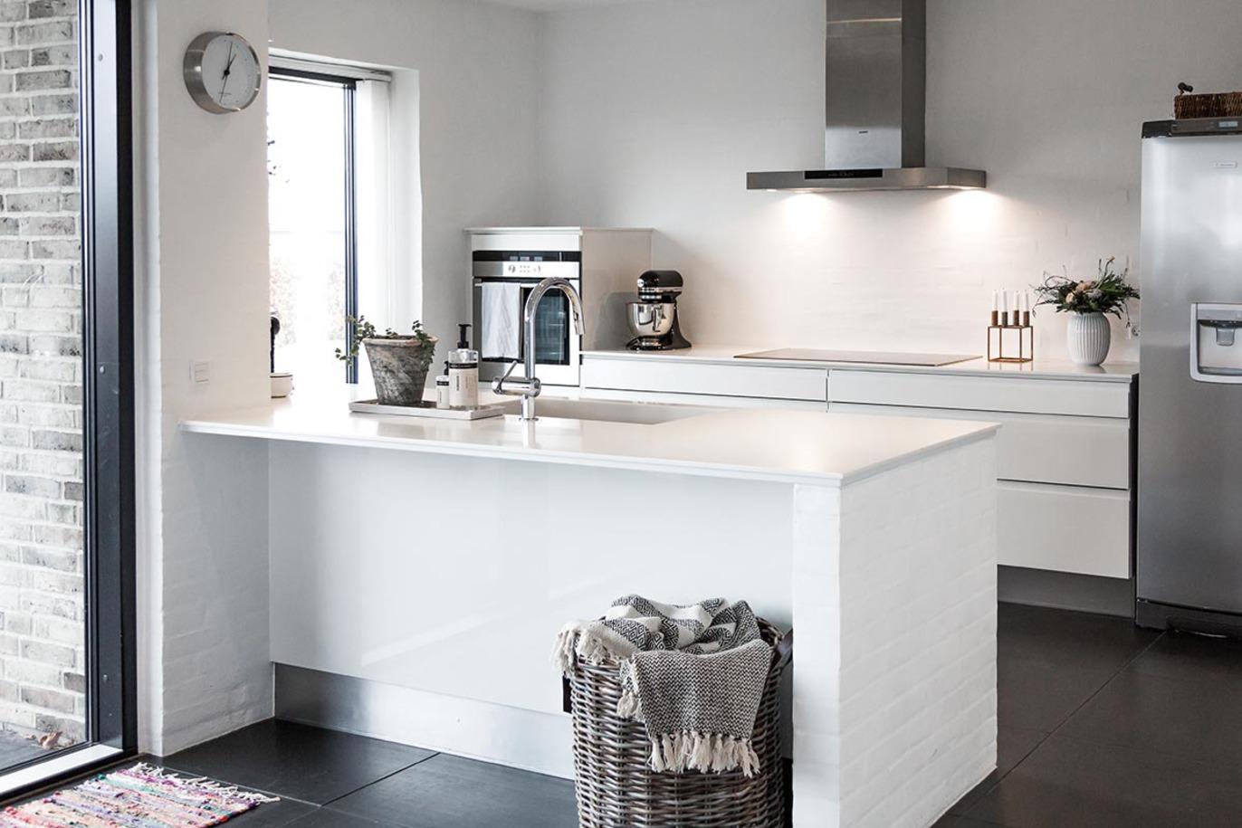 Moderne køkken med hvidt interiør, en stor ø, stålapparater og naturligt lys fra vinduerne.