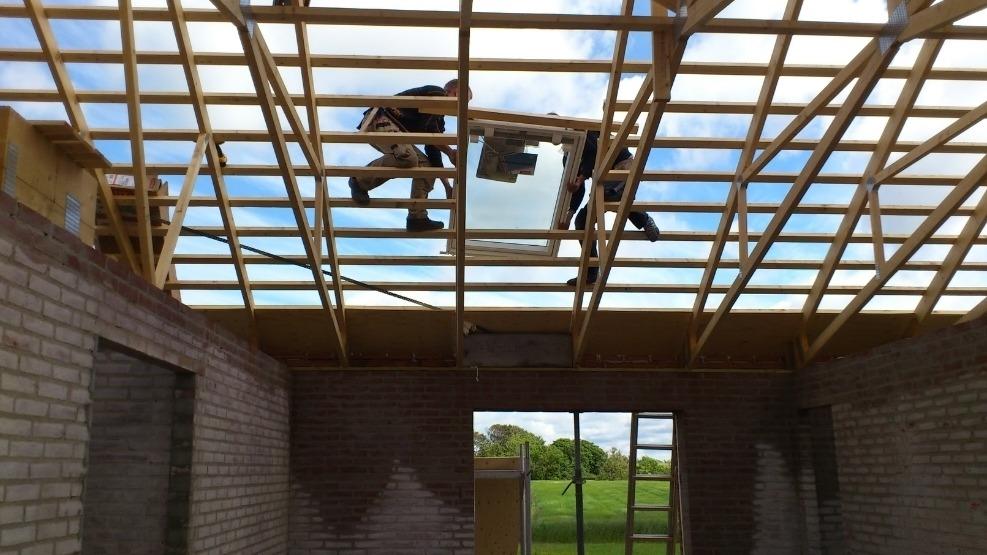 Bygningsarbejdere arbejder på taget af en nybygget bygning med synlige tagbjælker og åbent loft.
