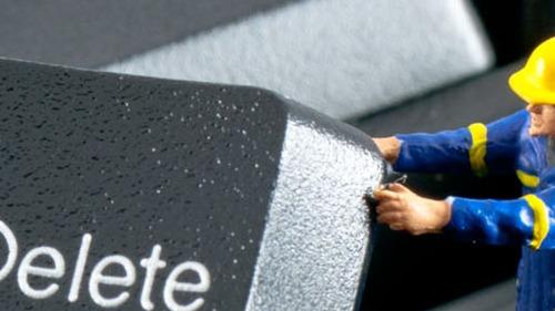 En miniaturefigur i arbejdstøj fjerner en tast fra et tastatur med teksten "Delete".