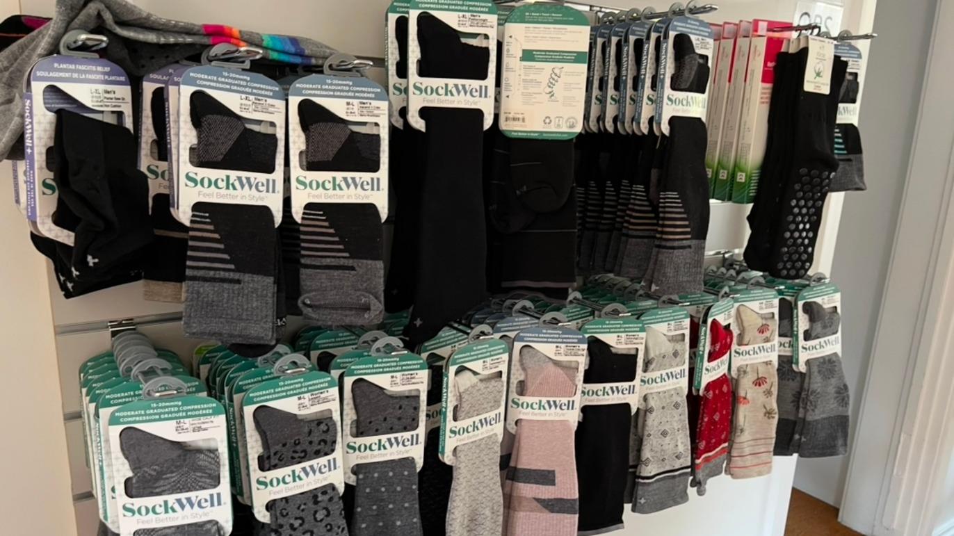En væg med forskellige sokker fra mærket SockWell, præsenteret i pakker med forskellige farver og mønstre.