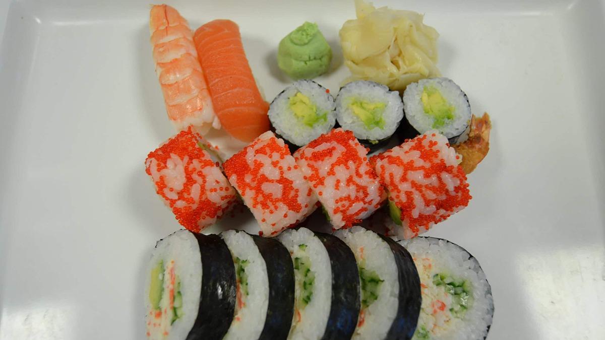 Farverig sushi anretning med nigiri, maki og wasabi på en hvid tallerken.