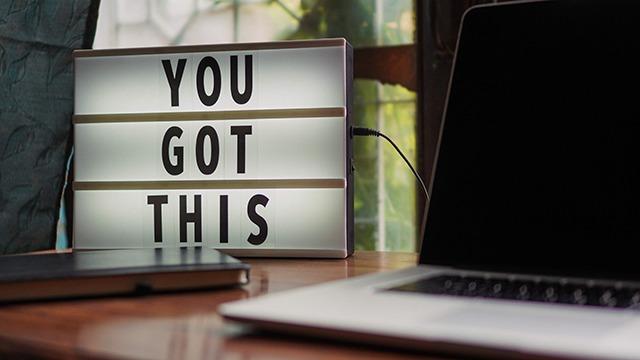 Lysboks med teksten "YOU GOT THIS" ved siden af en bærbar computer på et træbord.