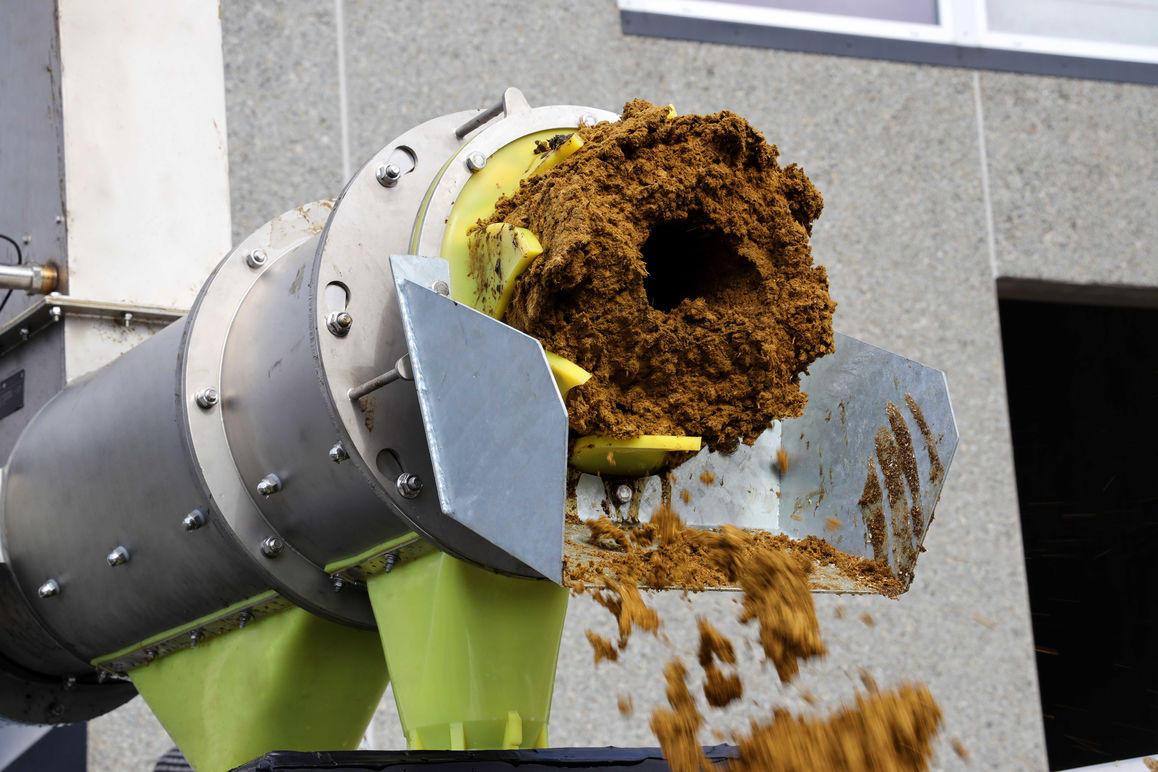 En maskine, der udskiller affaldsmateriale, med en stor klump af mudder, der falder ned fra udløbet.