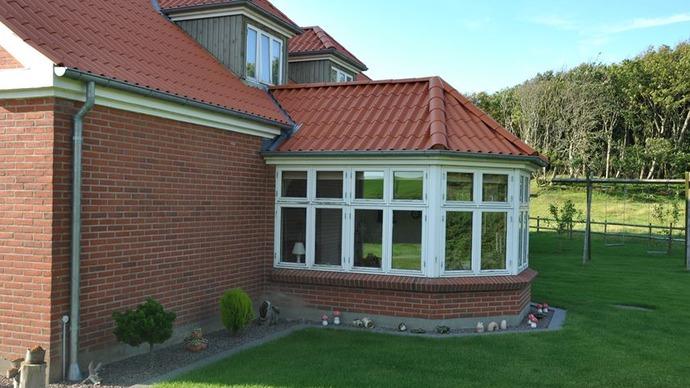 Et hus med en glasveranda, rød tagsten og grøn græsplæne i baggrunden.