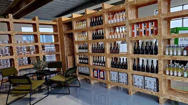 Indendørs butik med hylder af kork, fyldt med vinflasker og et lille siddeområde med stole og bord.