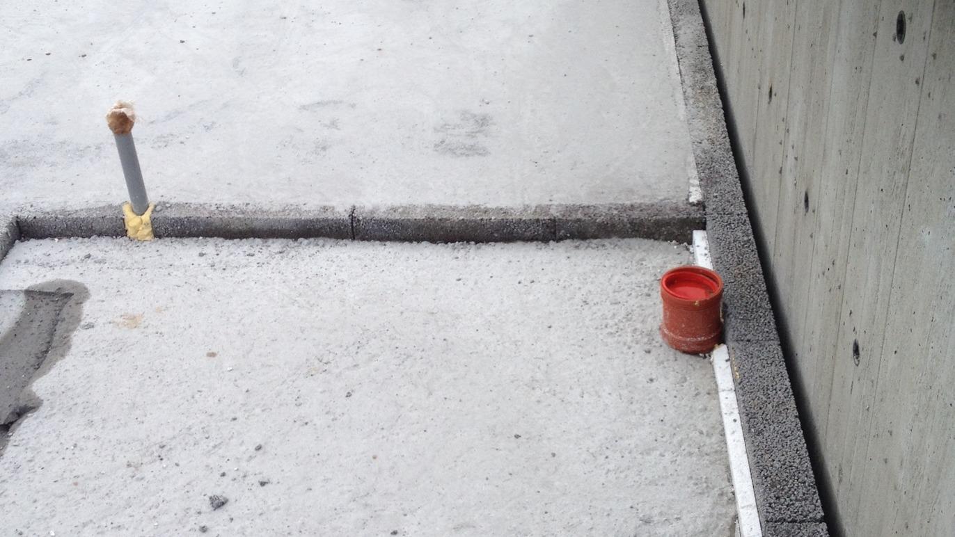Billede af en betonoverflade med en rød spand og en grå betonkant ved en væg.