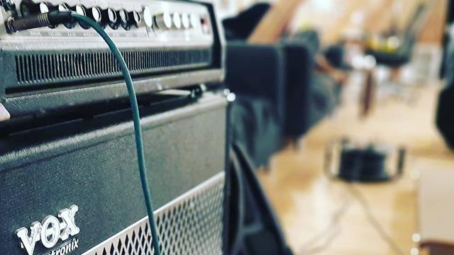 Forstærker fra Vox med en ledning, der er tilsluttet, i et musikstudie med bløde møbler i baggrunden.