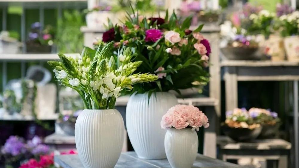 Vaser med blomster i en blomsterbutik, herunder hvide og lyserøde blomster i forskellige størrelser.