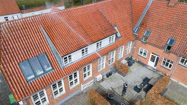 En person står på en gård og renser taget på en bygning med røde teglsten.
