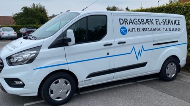 En hvid varevogn med teksten "DRAGSBÆK EL-SERVICE" og en blå linje, parkeret på en parkeringsplads.