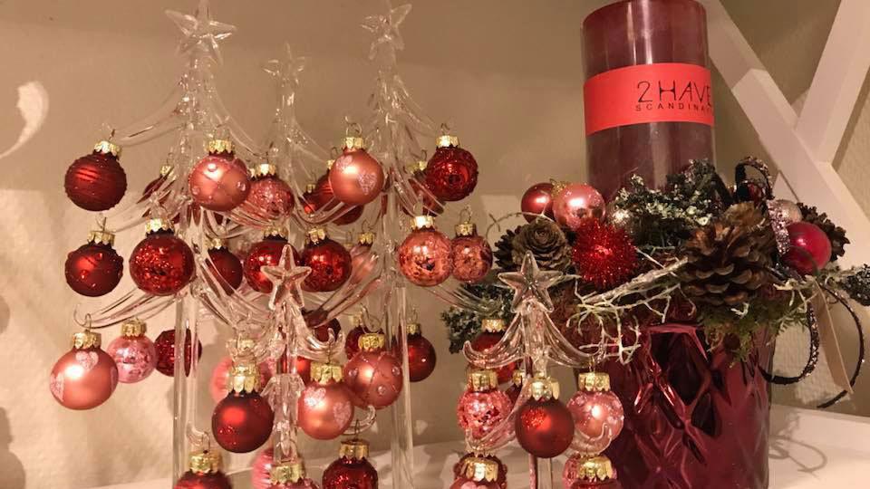 Julepynt med røde og lyserøde kugler, stjerner og en rød lysestage med gran og kogler.