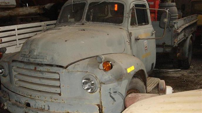 En gammel, rusten lastbil parkeret i en lade med slidte detaljer og en grå farve.