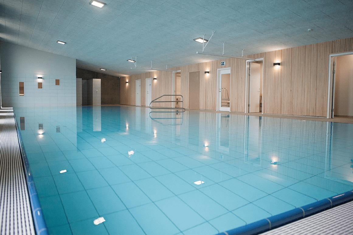 Indendørs swimmingpool med klart blåt vand og moderne belysning i et stilrent rum.
