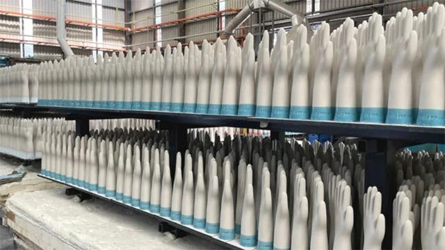 Række af hvide handsker på hylder i en fabrik, klar til distribution og brug.
